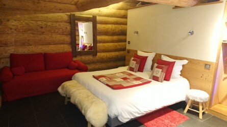 Grande chambre très confortable, avec un lit et un canapé. Ambiance chalet de montagne grâce aux couleurs rouges et motifs. chalet maramour chambre