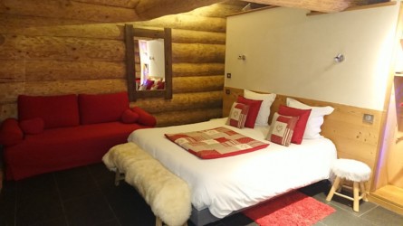Grande chambre très confortable, avec un lit et un canapé. Ambiance chalet de montagne grâce aux couleurs rouges et motifs. chalet maramour chambre